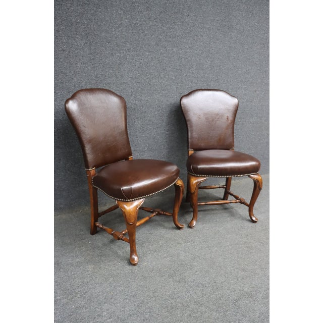 Pair of Theodore Alexander side chairs featuring brown leather upholstery, brass nailhead trim, and carved cherry frames...