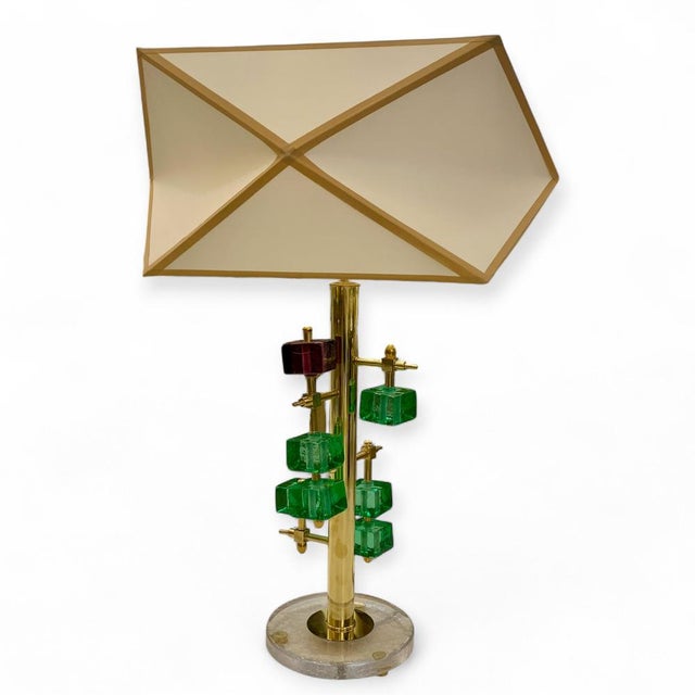 Table lamp with a circular Murano glass base and a cylindrical central structure in gilded brass. Lateral arms extend from...