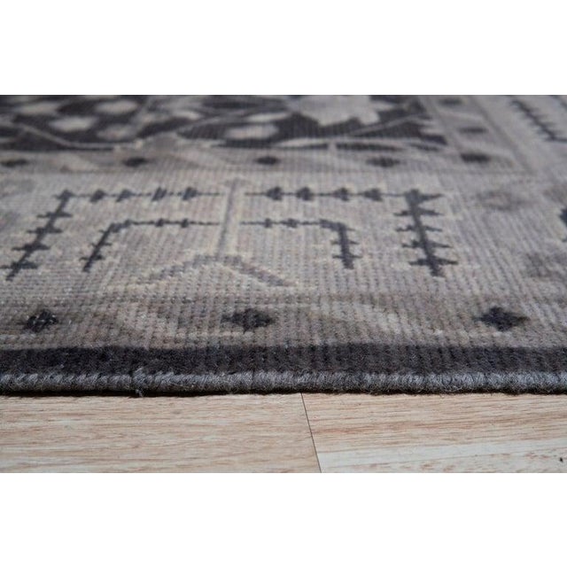 This gray hand knotted pile rug is crafted from wool and originates from India. It serves as a functional floor covering...