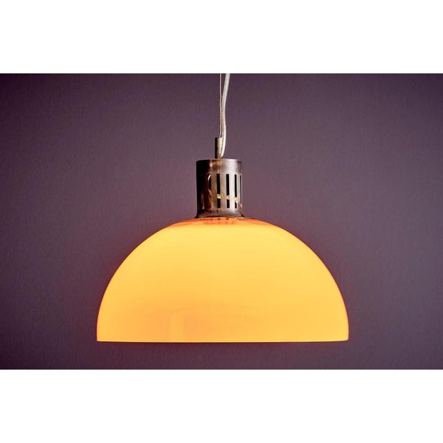 This Italian pendant lamp features a bright orange dome-shaped shade made of acrylic, paired with a perforated metal...