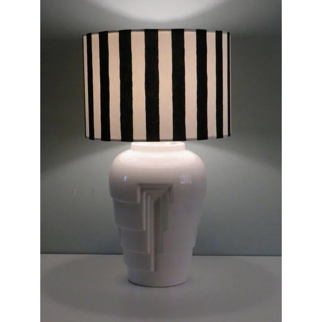 The white glazed lamp base features a skyscraper motif and a black and white striped custom-made lampshade. The height of...