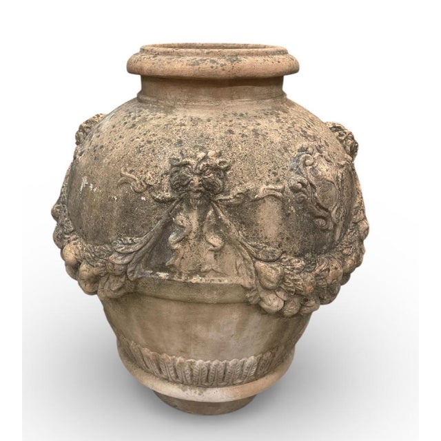 A striking and heavily weathered terracotta garden urn (or "orcia"), featuring rich Neoclassical relief carvings. This...