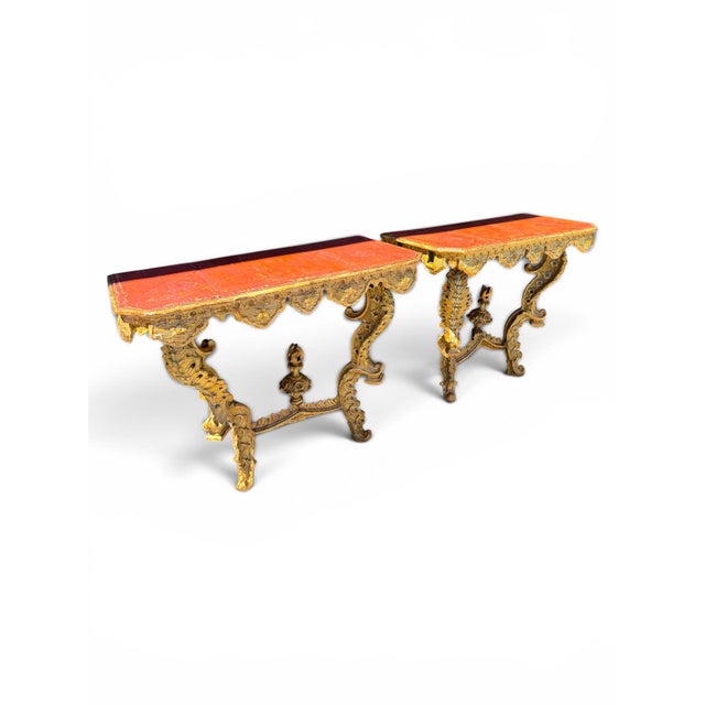 A rare and fine pair of 18th century Venetian giltwood console tables, each featuring a rectangular red-painted wood top...