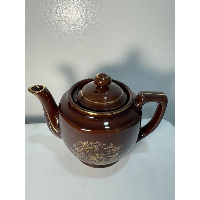 Vintage 1960s brown glazed ceramic teapot featuring an elegant gold floral design and fitted lid. Classic mid-century...