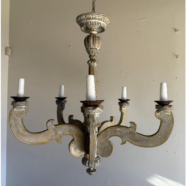 An elegant Italian six-light chandelier, mid-20th century, crafted in carved wood with gracefully scrolling arms and...