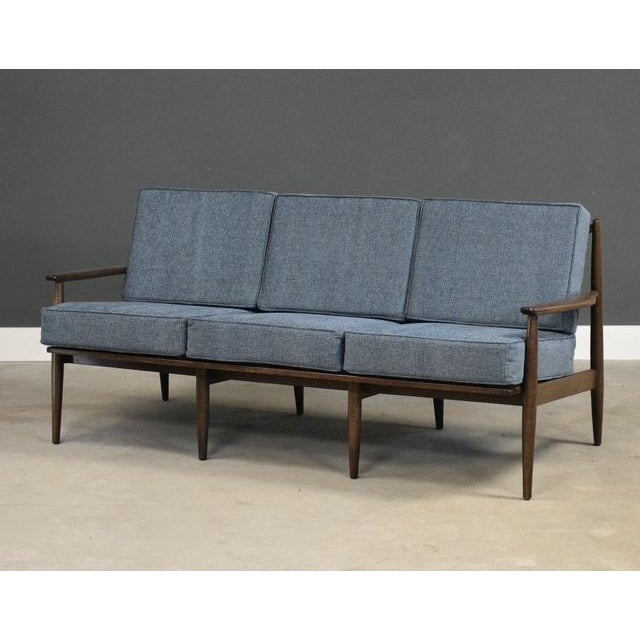 A mid century modern walnut color sofa with new blue fabric cushions made by Baumritter which was later bought out by...