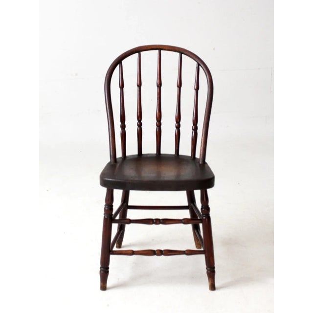 This antique Windsor-style chair features a gracefully arched back with finely turned spindles and a shaped seat that...