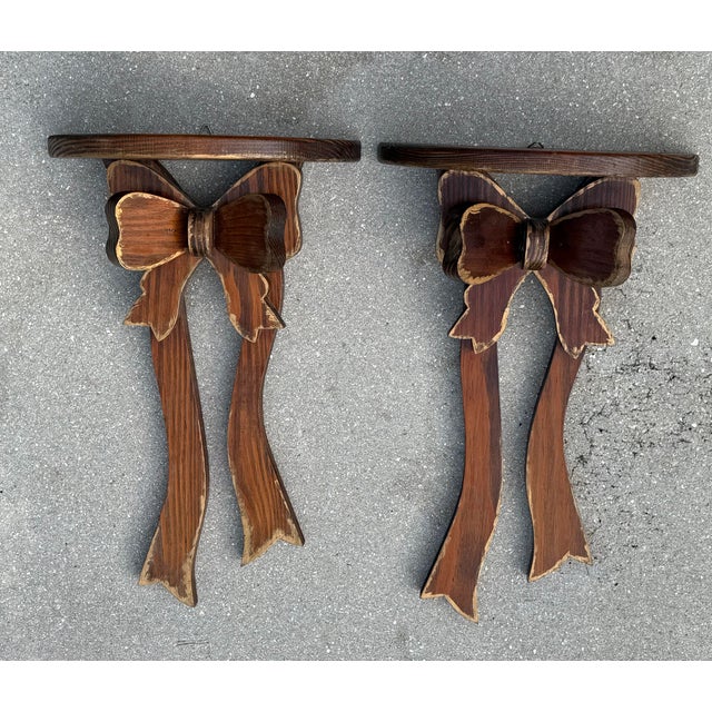 A charming pair of vintage folk art wall shelves featuring hand-carved oversized bows with long flowing ribbon tails....
