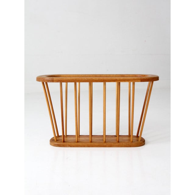 A mid-century wood magazine rack with a sculptural, open spindle form and softly rounded edges. Its elongated oval frame...