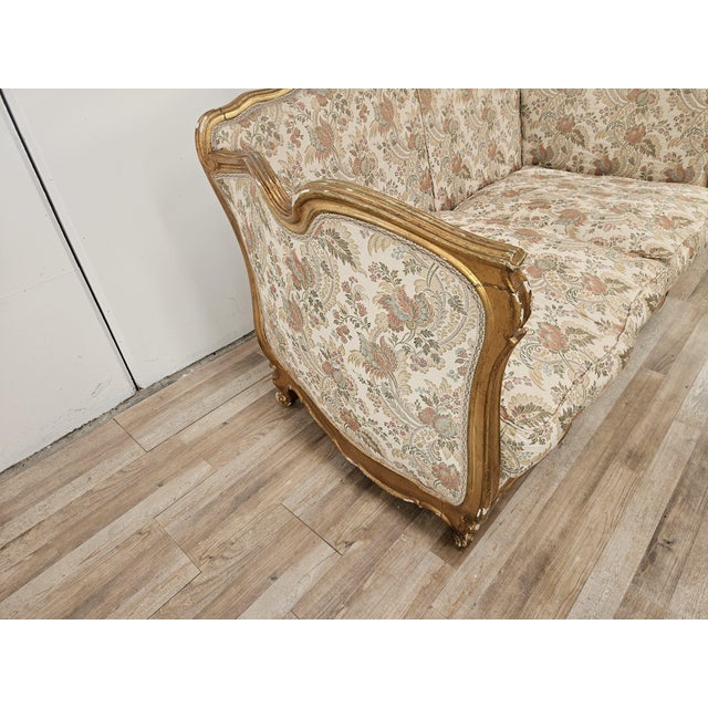 An elegant vintage two-seater sofa, featuring a contoured and richly decorated wooden frame with a gold finish and sinuous...