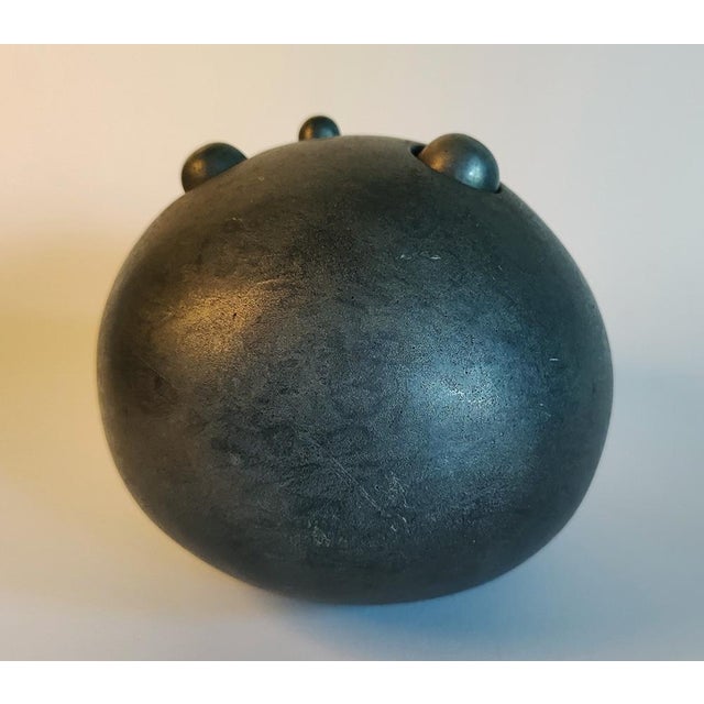 This cast metal sculpture contrasts industrial aesthetic with the fragility and grace of new blooms as they emerge from a...