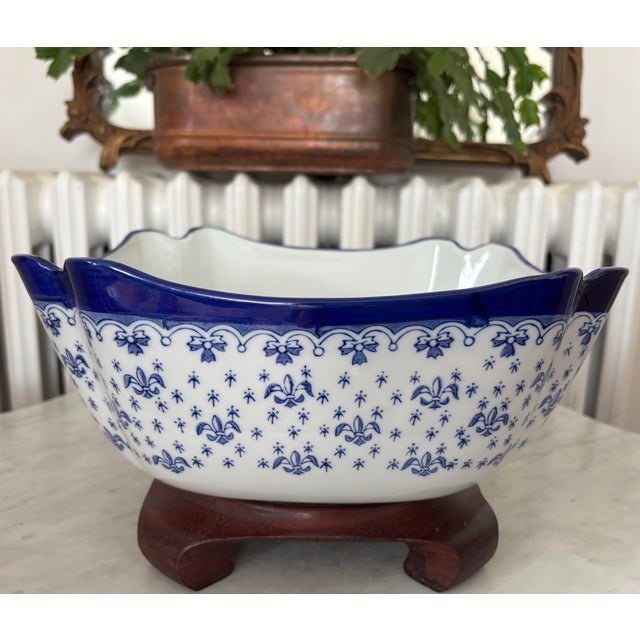 An eye-catching blue and white porcelain bowl with Fleur-de-lis design, elevated on a wooden stand. Circa late-20th...