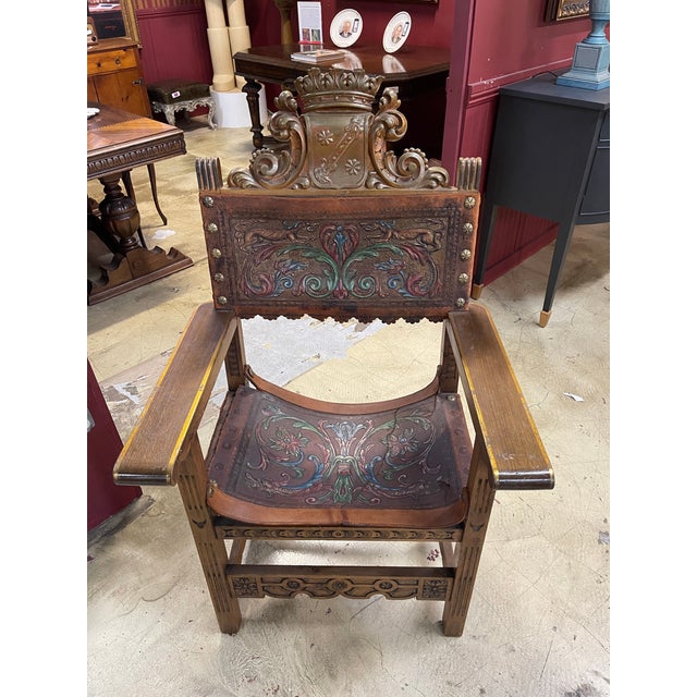 This ornate armchair features tooled leather panels with vibrant floral motifs and a grand crown crest backrest, accented...