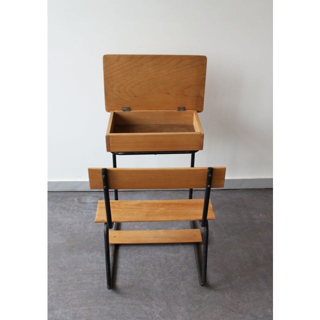 A wooden school desk with a black tubular metal frame that gives it a light and graphic look. The wooden seat, footrest,...