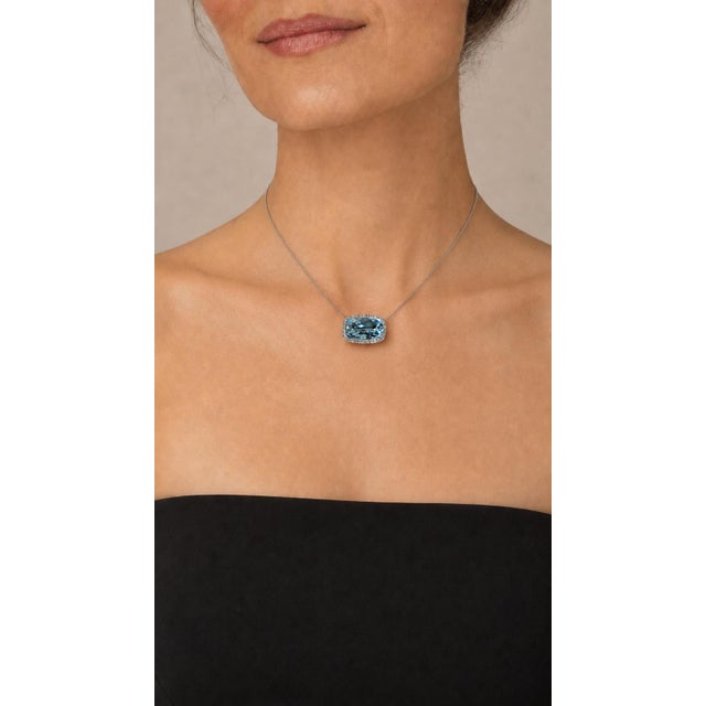 A luminous cushion-cut aquamarine weighing approximately 20 carats is framed by approximately 2.00 carats of round...