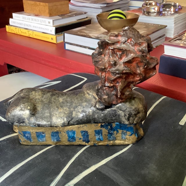 Red haired sphinx lounging on top of blue and gold leaf base. Made of plaster