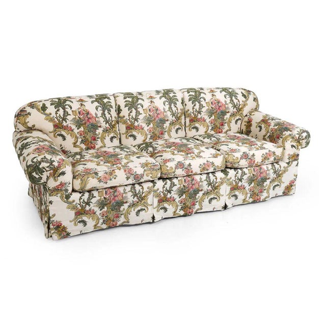 A traditional three seat sofa upholstered in a Jean Monro chinoiserie inspired floral fabric featuring stylized figures,...