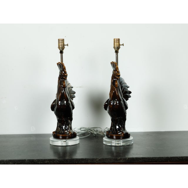 Two French pottery rooster table lamps from the mid 20th century, with dark patina and lucite bases. reated in France...
