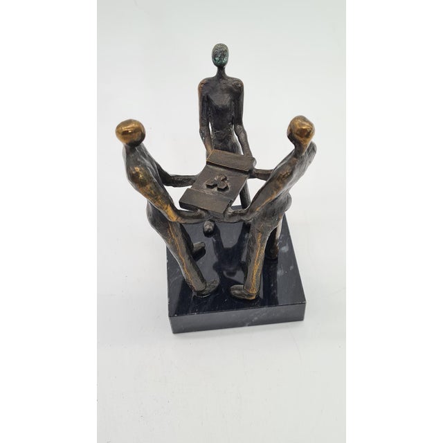 An artistic bronze figurine (bronze alloy) depicting three stylized figures holding a common object, symbolizing...