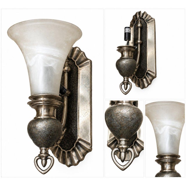 A vintage wall sconce with an elegant frosted glass shade, Tuscan Gold metal, and an ornate decorative backplate. The...