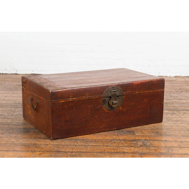 A Chinese Qing Dynasty period red painted paper bound trunk from the 19th century with traditional brass medallion...