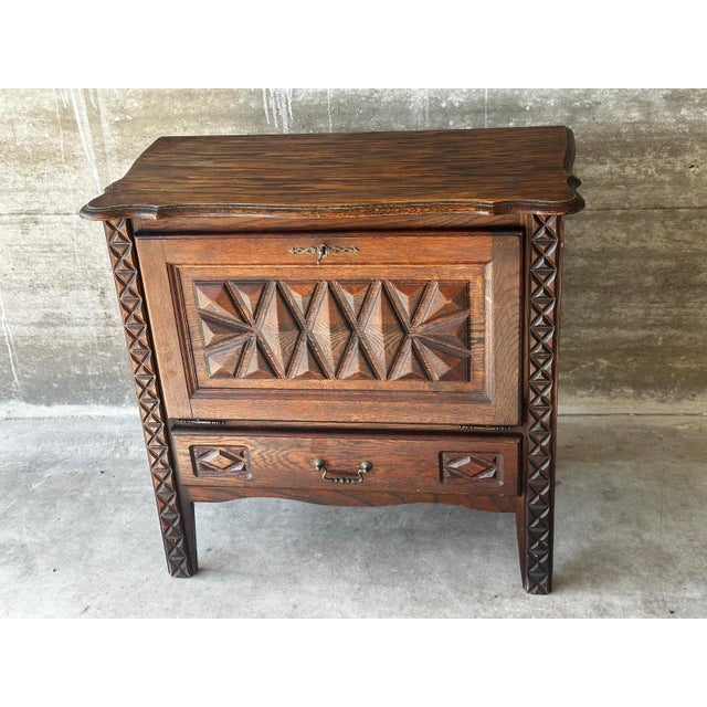 Small carved oak storage cabinet, circa 1930. It opens with a lockable drop-front, featuring an interior shelf and a wide...