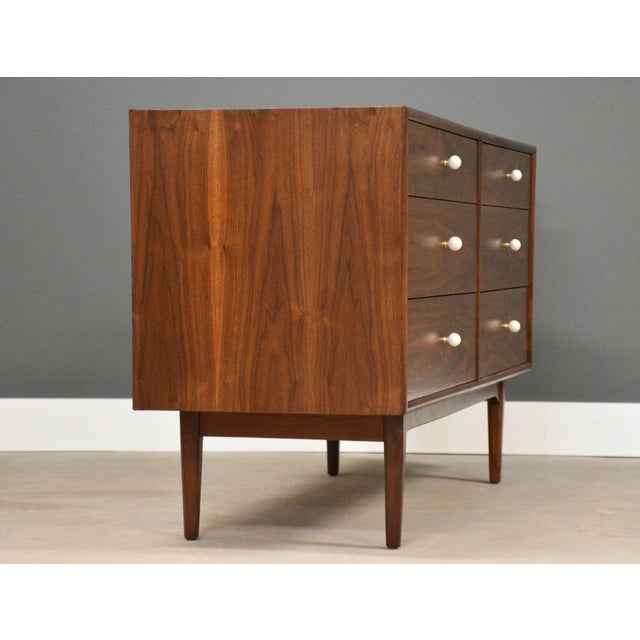 A mid century modern walnut Declaration six drawer dresser with white porcelain knobs and brass spacers designed by Kipp...
