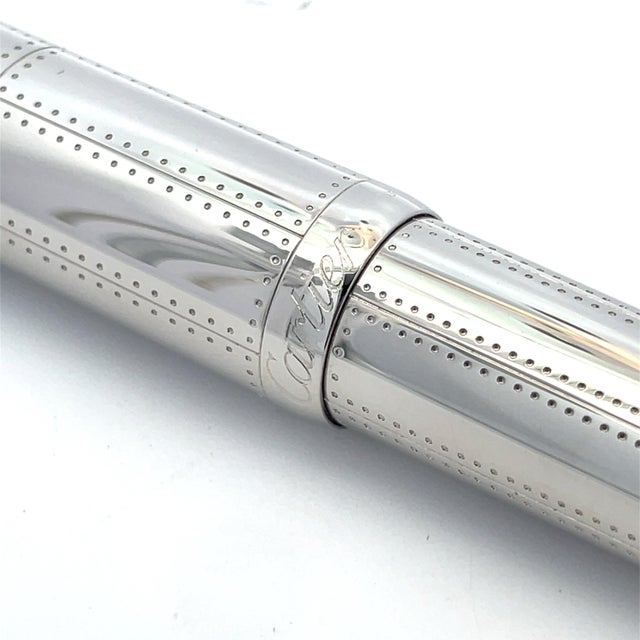 Elegant Cartier rollerball pen in a palladium finish with signature rivet pattern and blue resin cabochon on the cap. This...