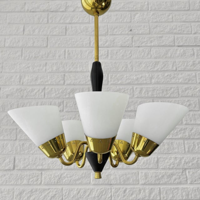 A Scandinavian modernist chandelier crafted from brass, featuring five curved arms supporting conical opal glass shades....