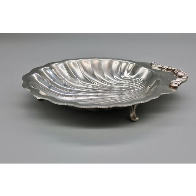 A lovely vintage silverplate shell-form dish, with a fluted clam shell bowl raised on small feet and a scrolled crest...