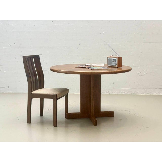 A striking round vintage dining table made of oak, likely from the 1970s. The design combines a solid, sculptural...