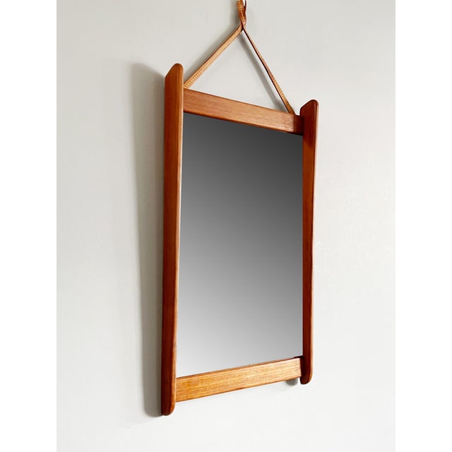 A wall mirror with a teak frame is for sale 1960s with leather strap suspension Mass HWD: 5.5 x 36.5 x 63 cm The object...