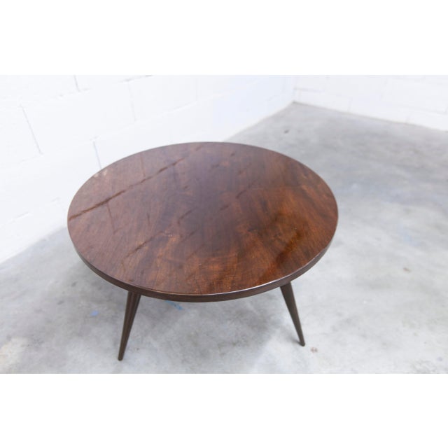 A 1960s tripod coffee table in varnished mahogany. The tabletop is clean and has a beautiful varnished finish. There are a...