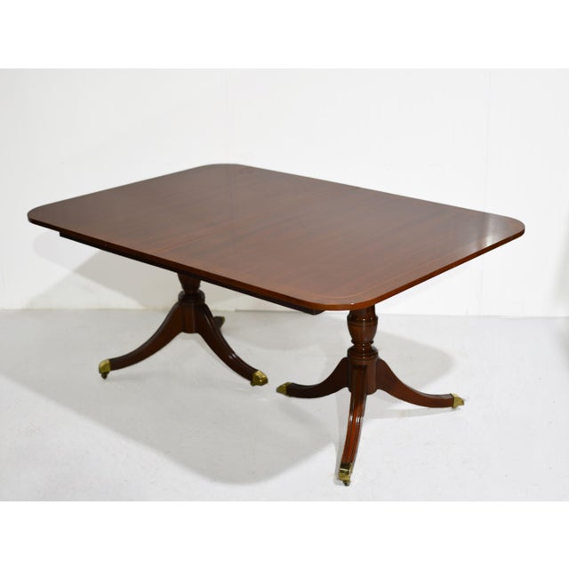 Mid century Georgian dining table by Kindel Furniture features a warm brown wood finish and a rectangular banded top with...