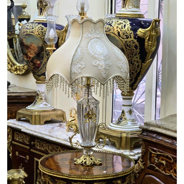 Elegant vintage French-style beige table lamp featuring a beautifully cut crystal body accented with ornate gold leaf...