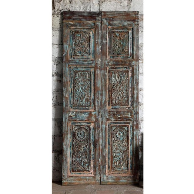 A striking antique Indian carved wood door panel, adorned with an intricate blue floral motif that brings timeless...