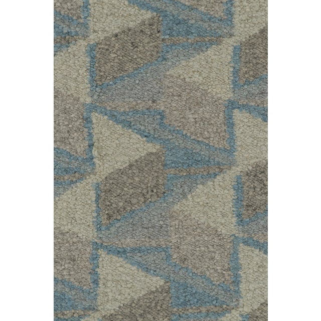 This 9x10 Scandinavian rug showcases an interlocking geometric layout rendered in soft blue, beige, gray, and charcoal....