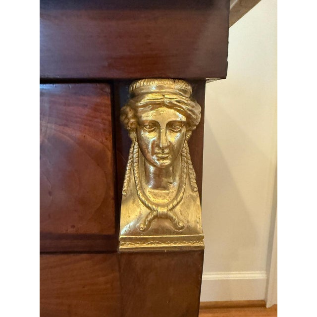 This showpiece three drawer chest features a marble top, flame mahogany, and brass figural accents. Legs terminate in claw...