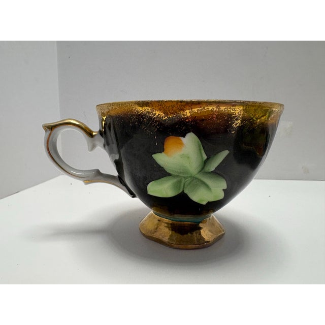 Vintage hand-painted Japanese teacup and saucer featuring a bold fruit design on a black ground with rich gold detailing....
