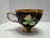 Vintage hand-painted Japanese teacup and saucer featuring a bold fruit design on a black ground with rich gold detailing....