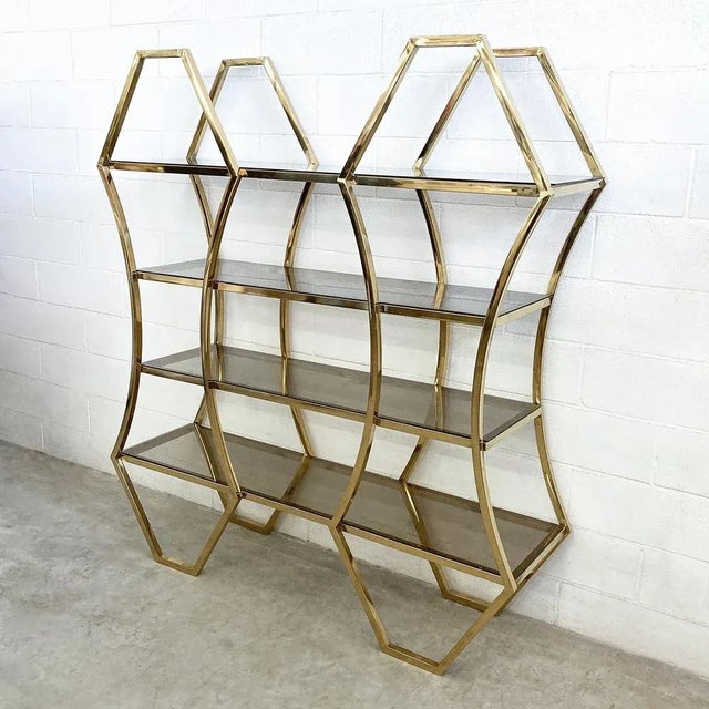 Elegant shelves in gilded brass tubular with square section with 4 fumè glass shelves. This library with sinuous geometric...