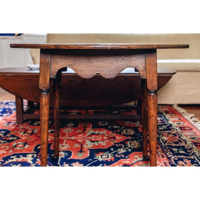An antique Queen Anne style oak side or tea table with a warm wood finish, oval top, scalloped apron and turned and...