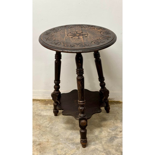 A charming antique English tripod table, distinguished by its rounded top adorned with exceptional carved detailing in a...