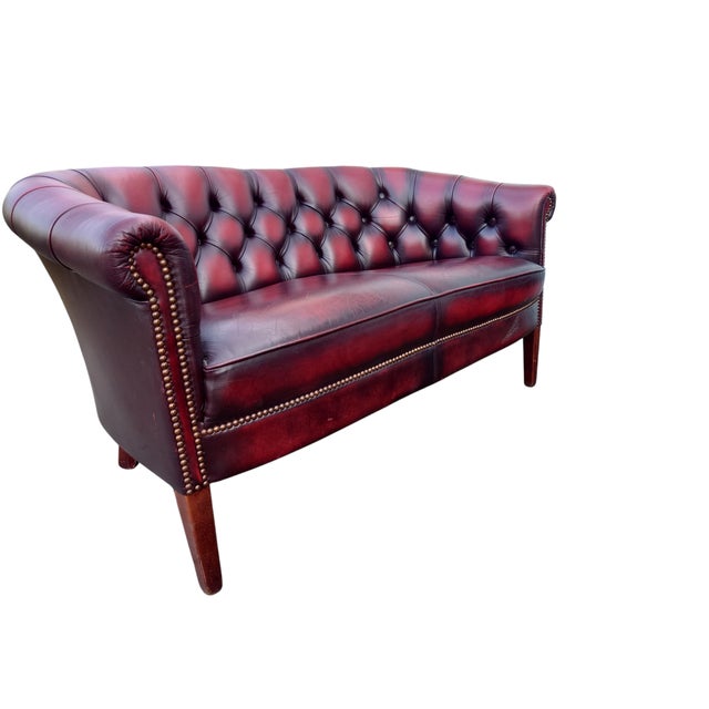A charming two-seater in classic Chesterfield style, upholstered in deep oxblood red leatherette with a rich patina and...