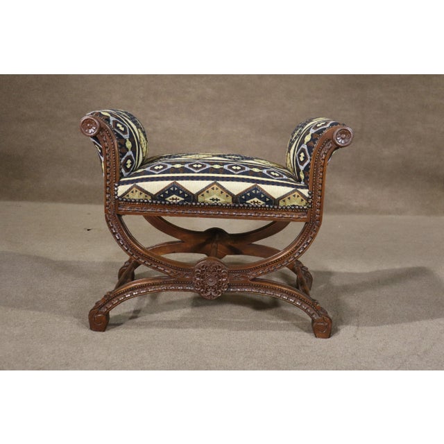Antique carved frame bench with criss-cross base and scrolling arms. Upholstered seat and arms, with hand carved...
