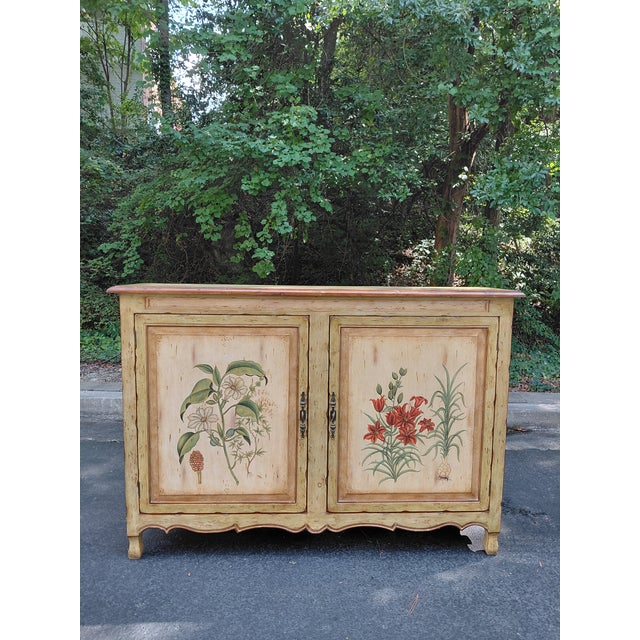Charming French Provincial-style sideboard featuring a softly distressed warm cream finish with contrasting wood trim. The...