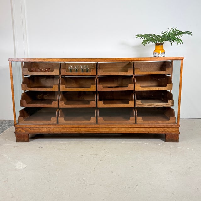 This impressive shop counter from Germany (ca. 1930s–1950s) features a solid oak frame and 16 stepped drawers fitted with...