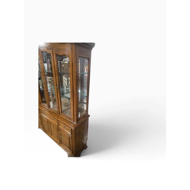 Elegant vintage china cabinet by Thomasville featuring a warm oak finish, architectural detailing, and a gracefully...