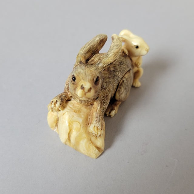 A finely carved 1930's Japanese bone netsuke depicting a mother rabbit with her young, rendered in a tender and animated...