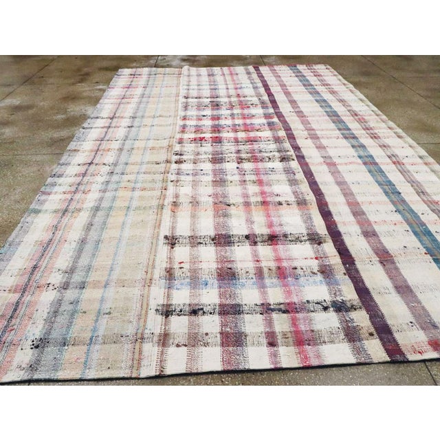 This Mid-20th century Turkish Flatweave Kilim rug, features a vibrant plaid-inspired design woven in soft, naturally faded...